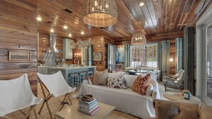 A cozy cabin interior with a wooden ceiling, a dining area, and a living room furnished with a sofa and chairs. - 3br/3.ba With Dock, Deck/balcony and Fireplace (Santa Rosa Beach)