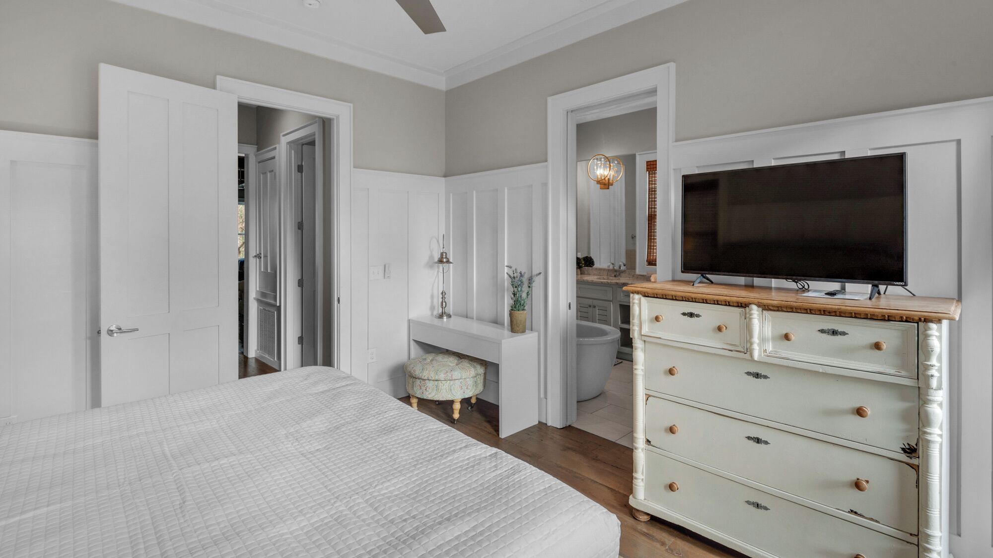 Un dormitorio con una cama grande, un aparador, un televisor y un baño visible a través de una puerta abierta.