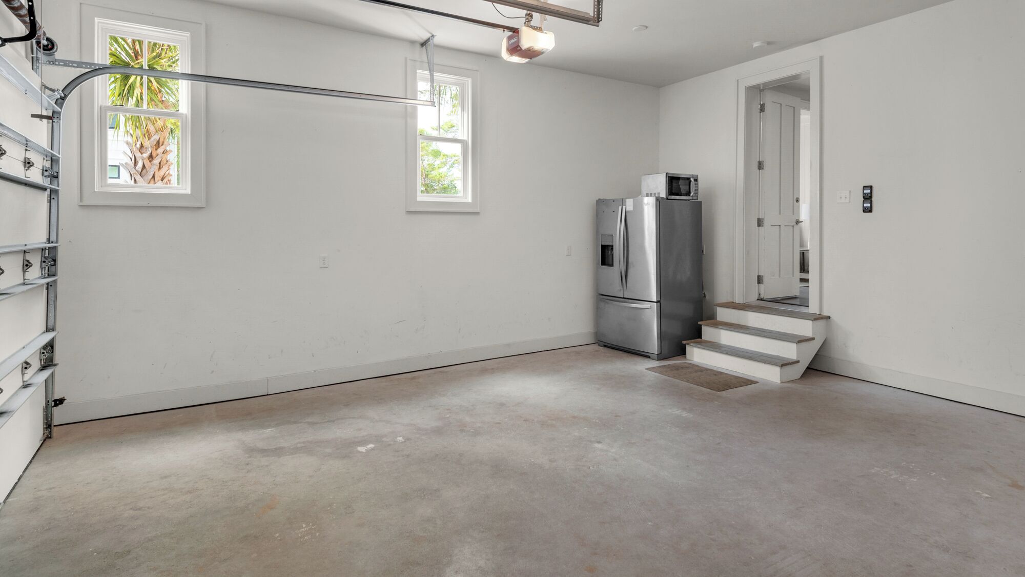 A spacious, unfinished room with a large window, a built-in refrigerator, and a staircase leading to another level.