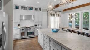 A modern kitchen with white cabinetry, a large island, stainless steel appliances, and a view of the outdoors. - 4 Minutes to Beach + Community Pool ~ Stunning Modern Home for 12 (Santa Rosa Beach)