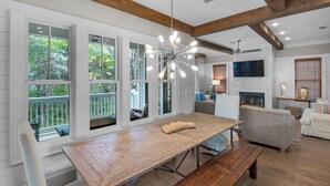 A spacious living area with a wooden dining table, a gray sofa, and a TV mounted on the wall. - 4 Minutes to Beach + Community Pool ~ Stunning Modern Home for 12 (Santa Rosa Beach)