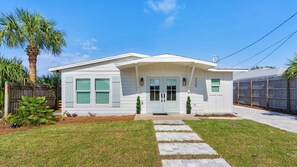 A single-story house with a front porch, a small front yard, and a wooden fence. - 4 Minutes to the Beach! Cute & Coastal With Room for 9 (Panama City Beach)