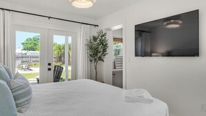 Une chambre à coucher avec un lit, un téléviseur fixé au mur et une vue sur l’extérieur grâce à une porte coulissante.