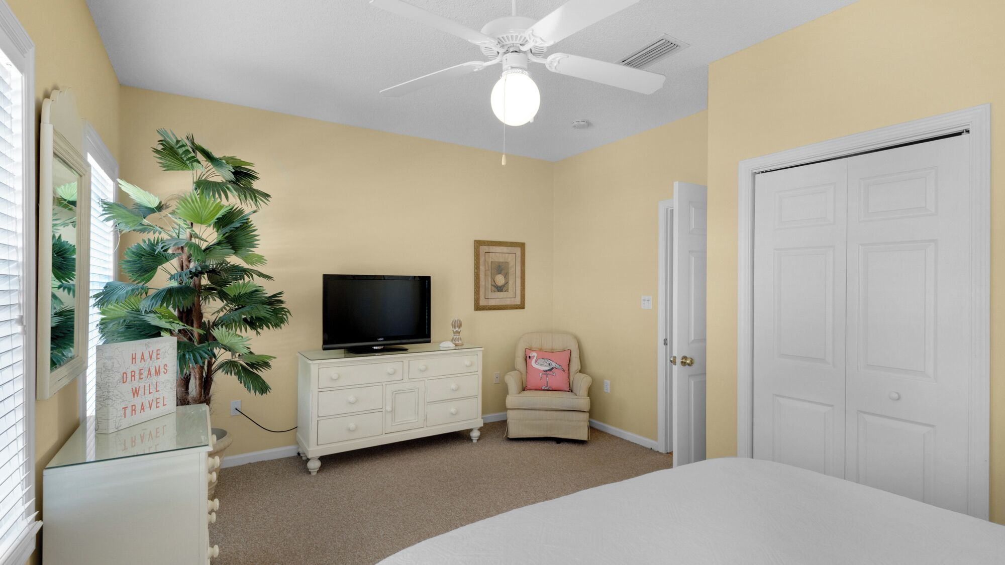 A bedroom with a bed, a dresser, a television, a chair, a door, and a ceiling fan.