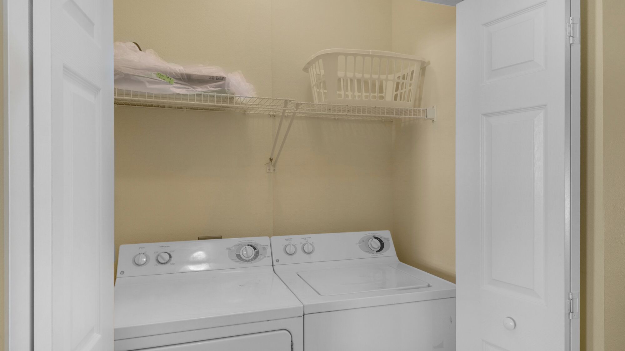 Un área de lavandería con lavadora y secadora, una puerta blanca y una cesta de ropa en un estante.