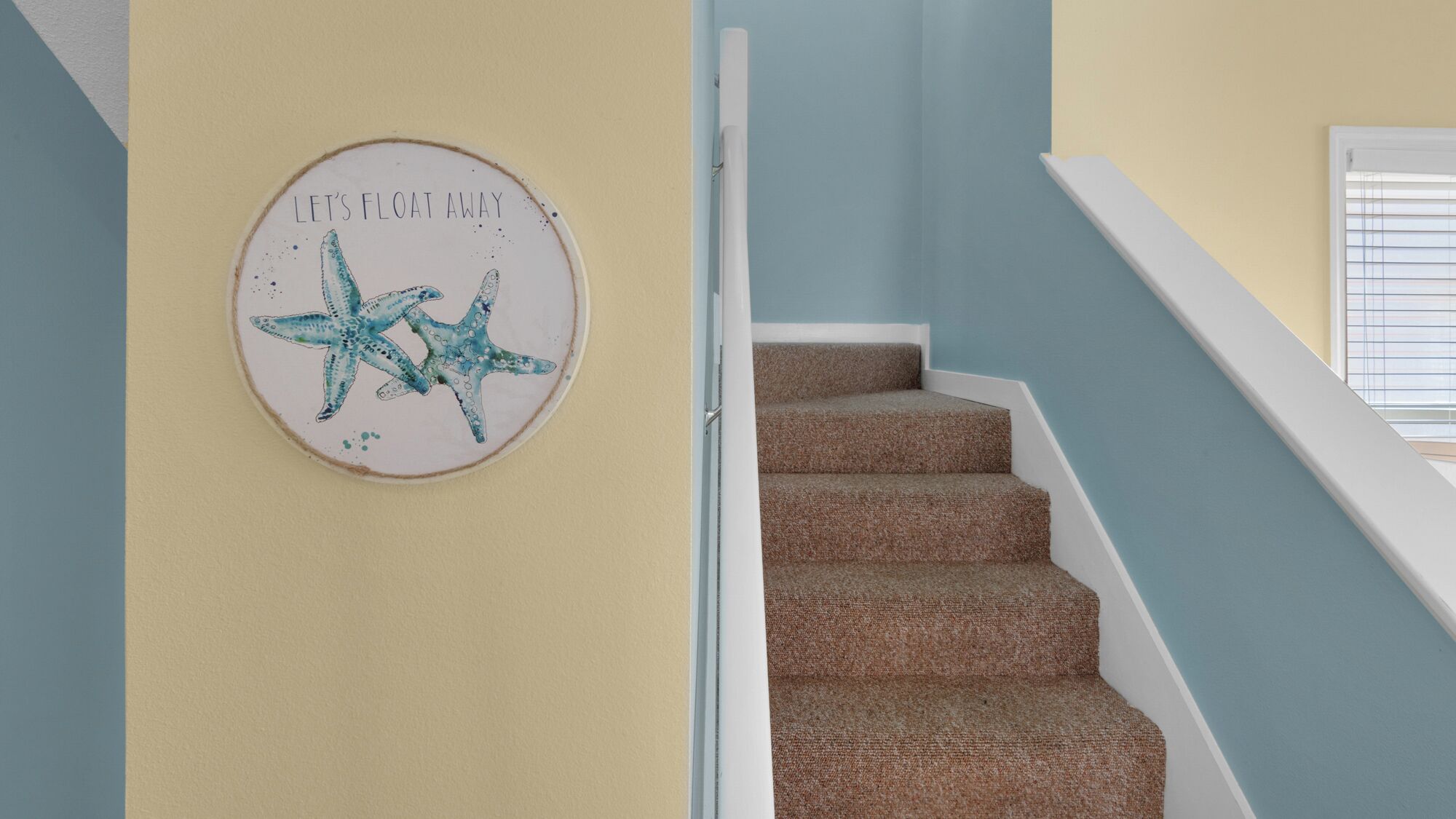 A staircase with a wall-mounted sign that reads 'LET'S FLOAT AWAY' and features a starfish illustration.