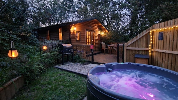 A wooden cabin with a hot tub, outdoor seating, and string lights. - Captivating 1-bed Cabin in Newmarket (Newmarket)