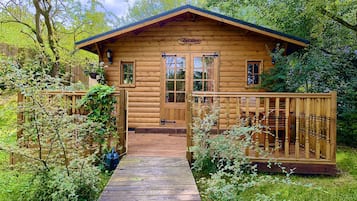 A wooden cabin with a porch and a wooden deck leading to the entrance.