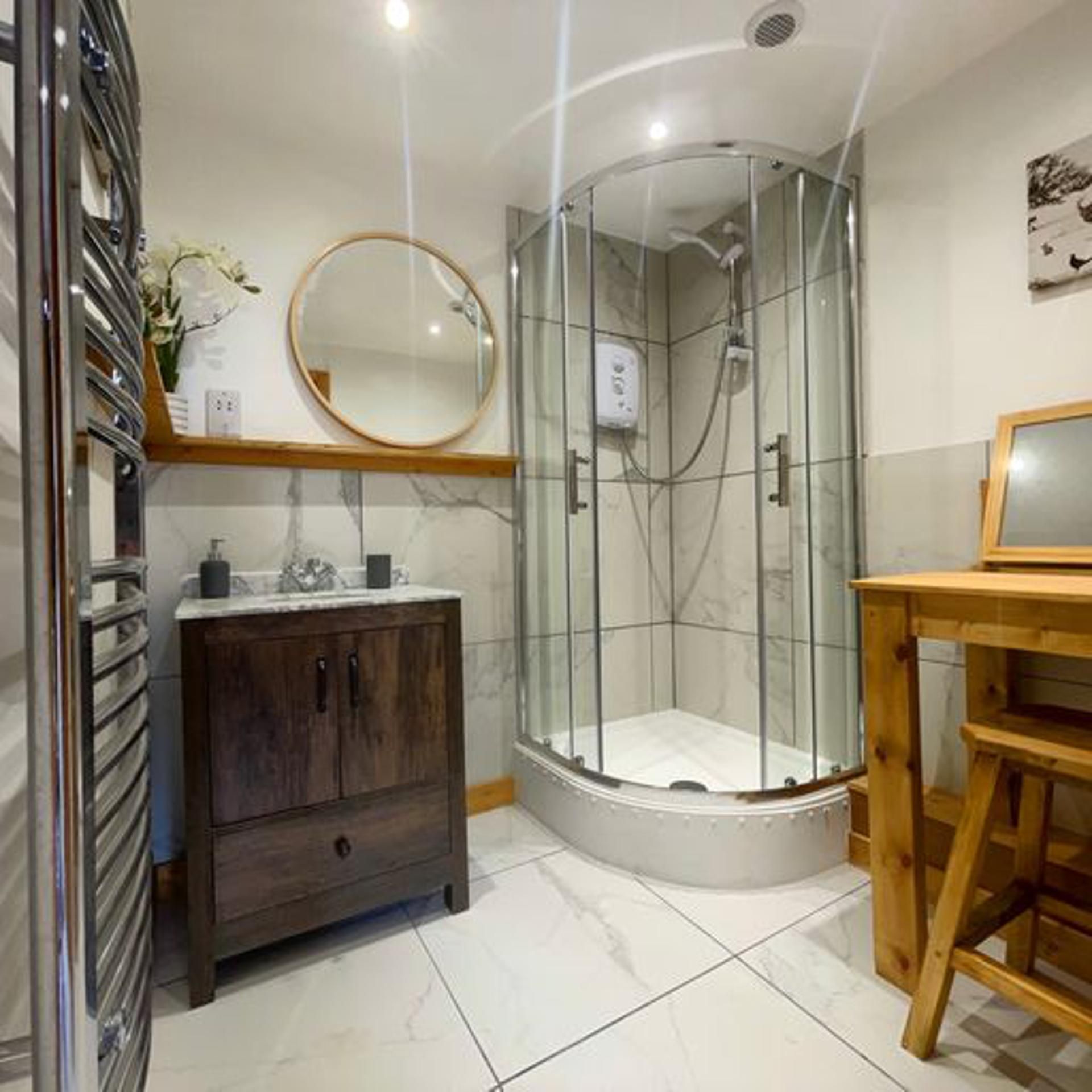 A bathroom with a glass-enclosed shower, a wooden vanity, and a marble-tiled floor.