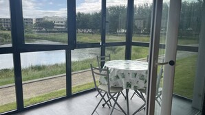 A room with large windows offering a view of a body of water, a grassy area, and buildings in the distance.