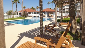 A poolside area with wooden lounge chairs, a pergola, and a view of a building with a red roof.
