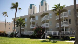 A multi-story residential building with balconies, a well-maintained lawn, and palm trees.