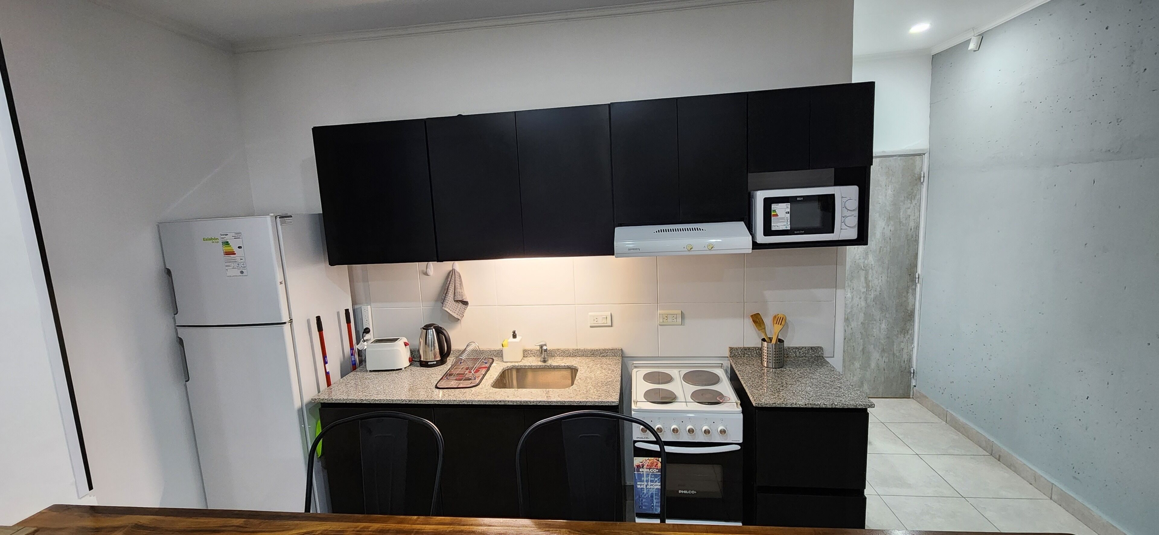 Una cucina compatta con mobili neri, un frigorifero bianco, un forno a microonde, un fornello e un lavello.