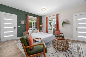 A bedroom with a bed, two chairs, a round coffee table, and a window with curtains.