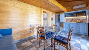 Interior de una cabaña de madera con mesa, sillas y pequeña cocina.