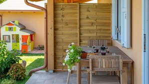 Una terraza de madera con una mesa y sillas, una casita de juegos al fondo y una cerca de madera.