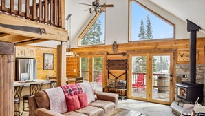 Een gezellig cabin interieur met houten details, een stenen openhaard en grote ramen met uitzicht op bomen.