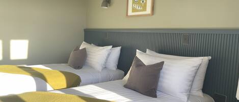 Habitación de hotel con dos camas, cabecero, lámpara de pared y un cuadro enmarcado.