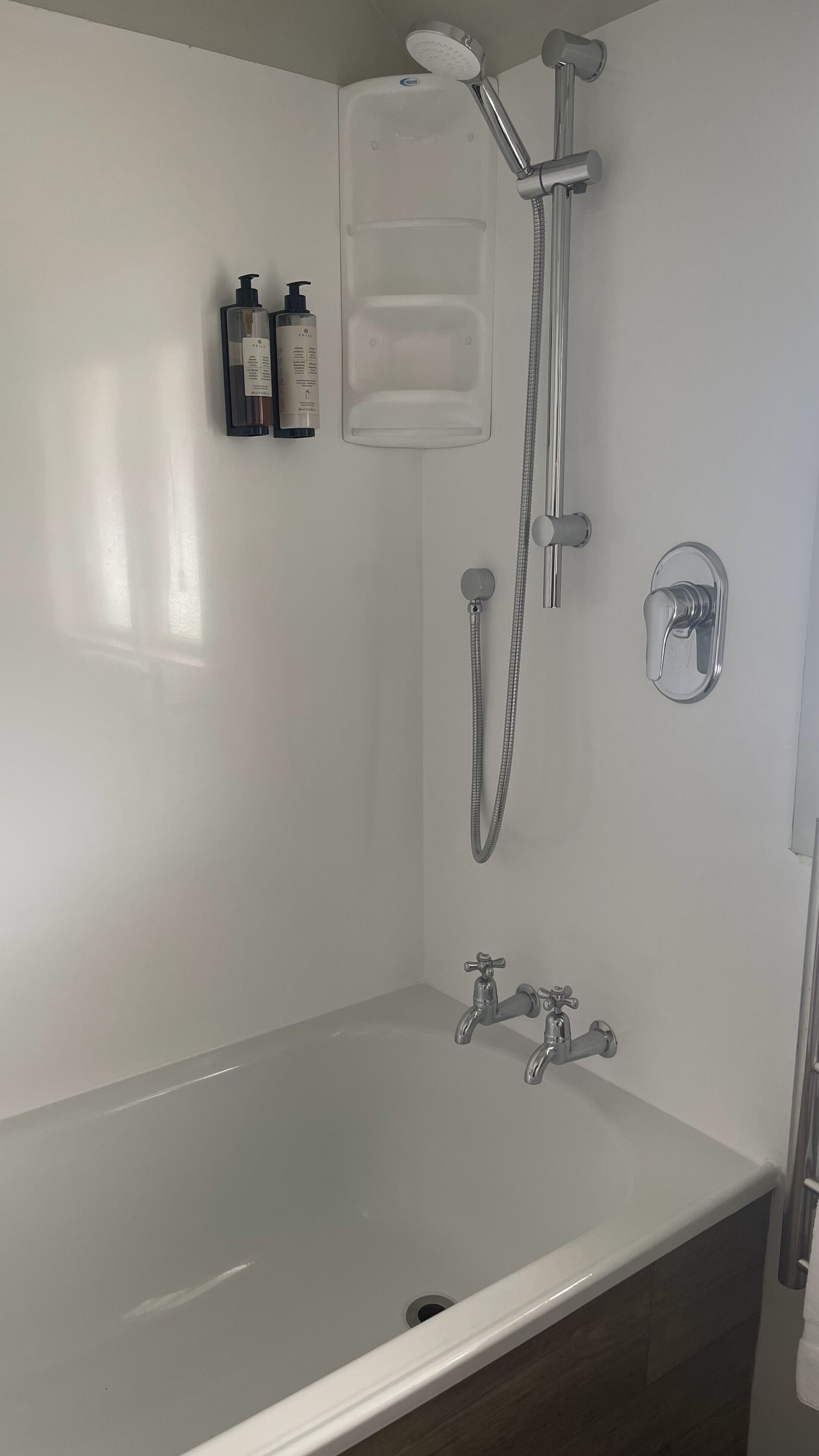 A modern bathroom with a white bathtub, a handheld showerhead, and two wall-mounted faucets.