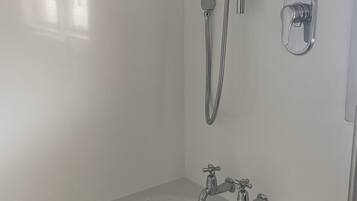 A modern bathroom with a white bathtub, a handheld showerhead, and two wall-mounted faucets.
