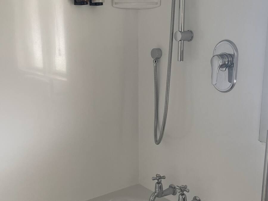 A modern bathroom with a white bathtub, a handheld showerhead, and two wall-mounted faucets.