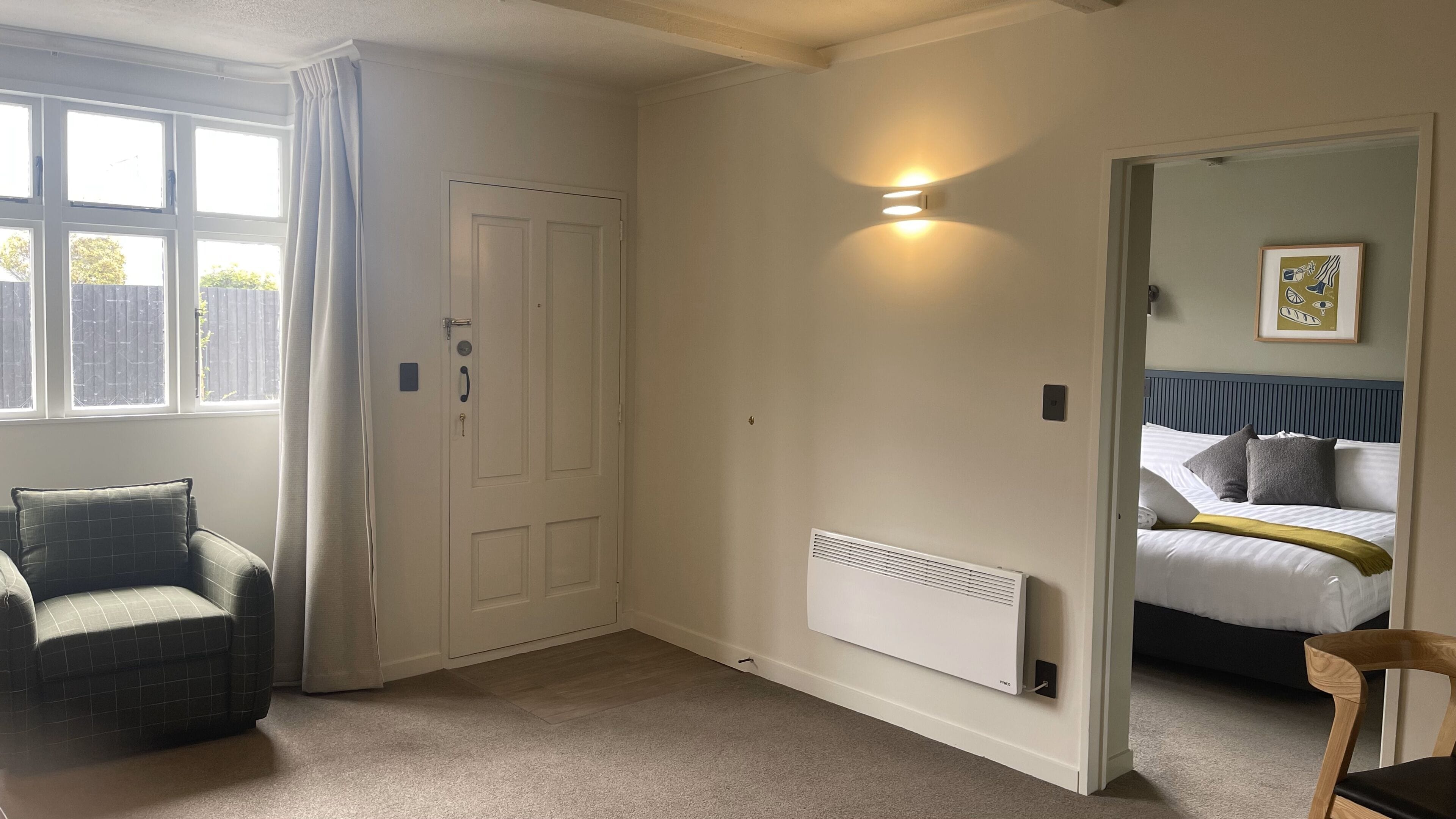 A room with a bed, a chair, a radiator, a door, and a window.