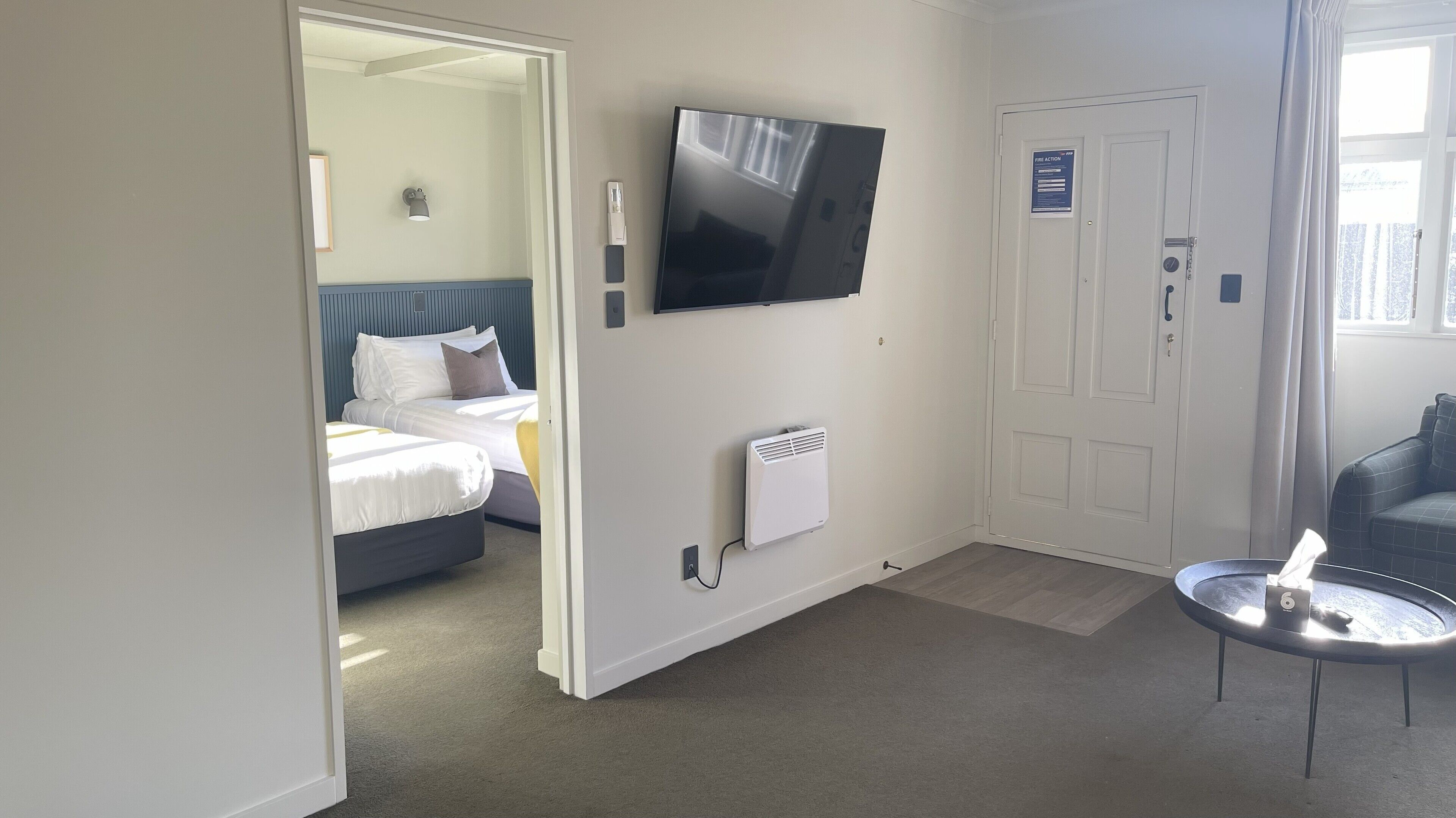 A hotel room with a bed, a TV mounted on the wall, a heater, and a small table with a laptop.
