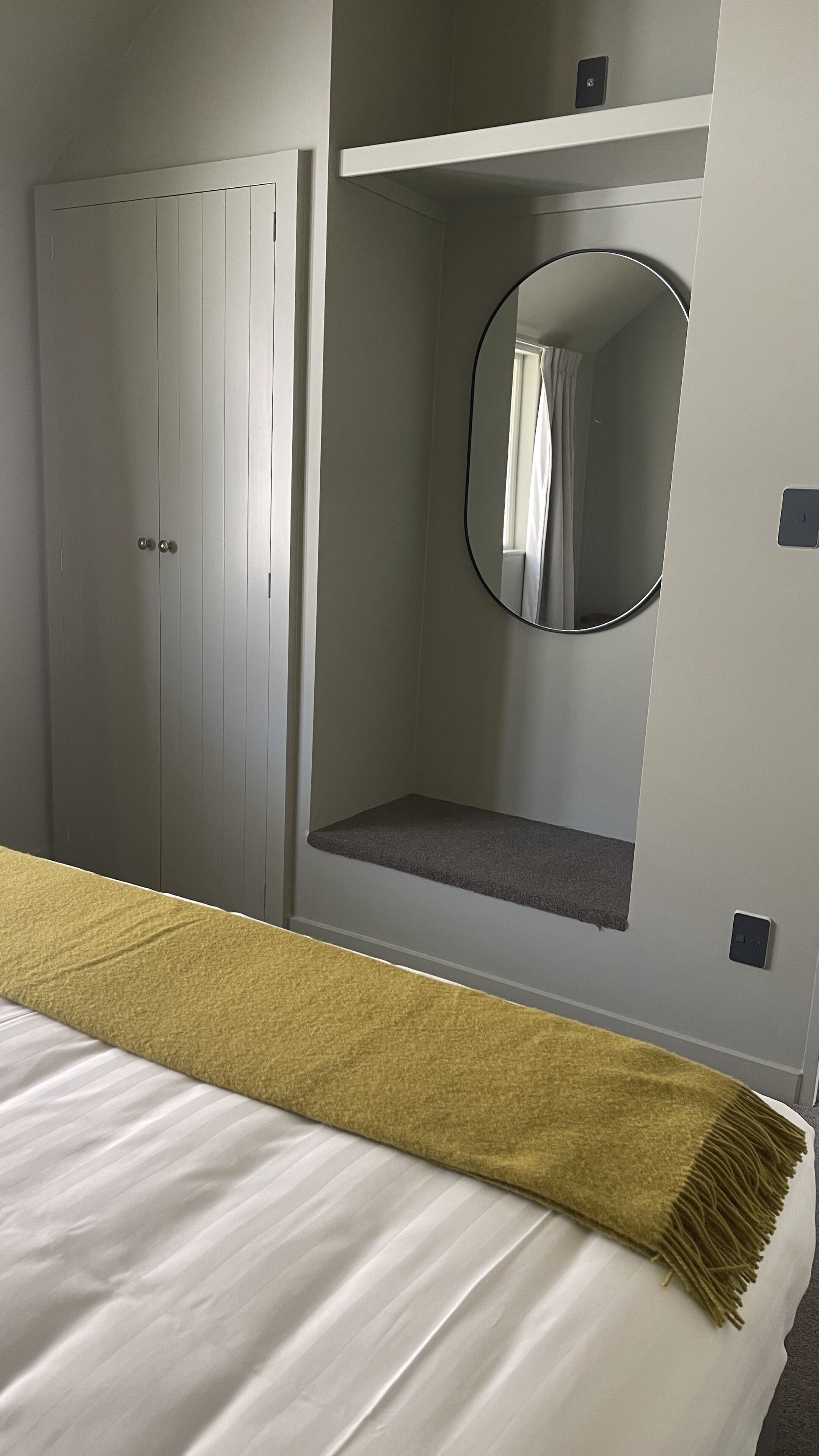 A bedroom with a bed, a wardrobe, a mirror, and a shelf.