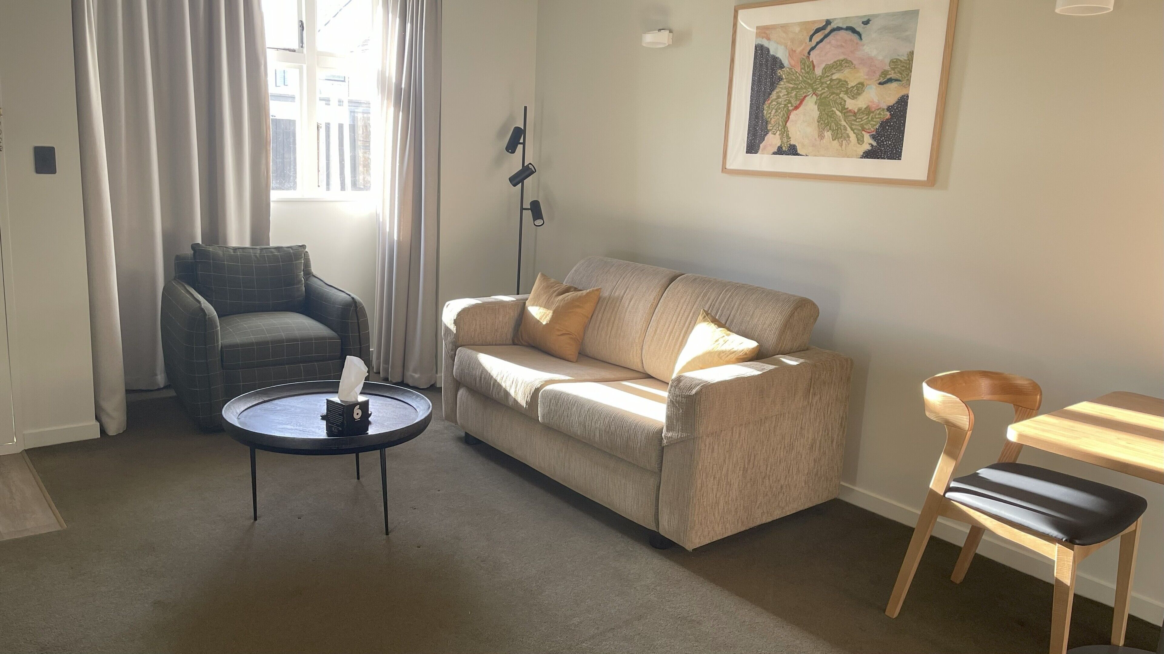 A living room with a sofa, a chair, a small table, and a painting on the wall.