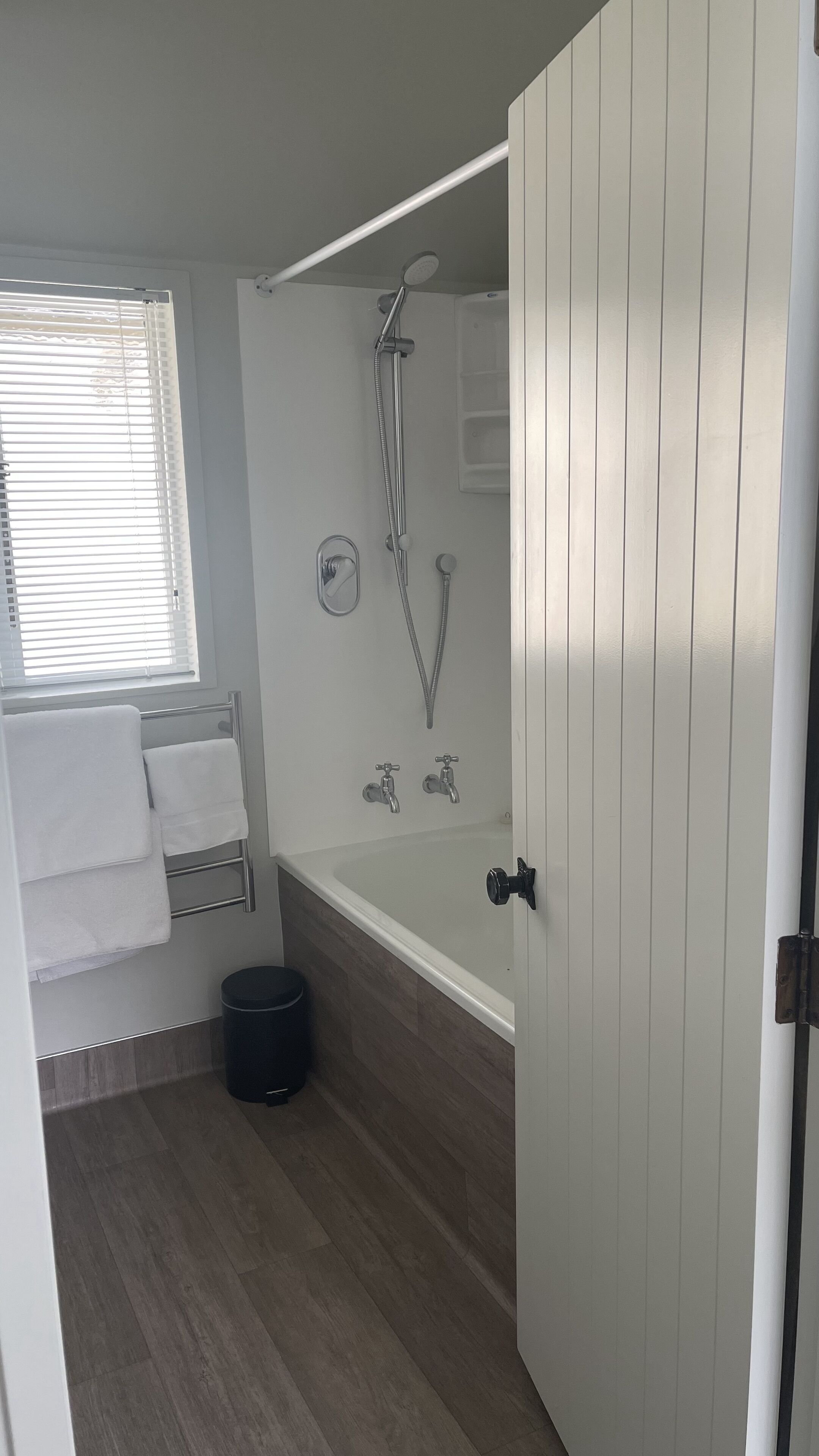 A bathroom with a shower, a bathtub, a toilet, and a window with blinds.