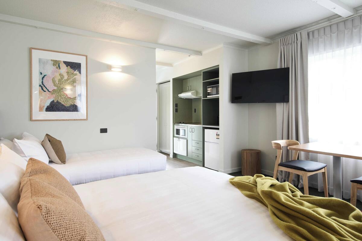 Een hotelkamer met een bed, een bureau, een stoel, een televisie en een kitchenette.