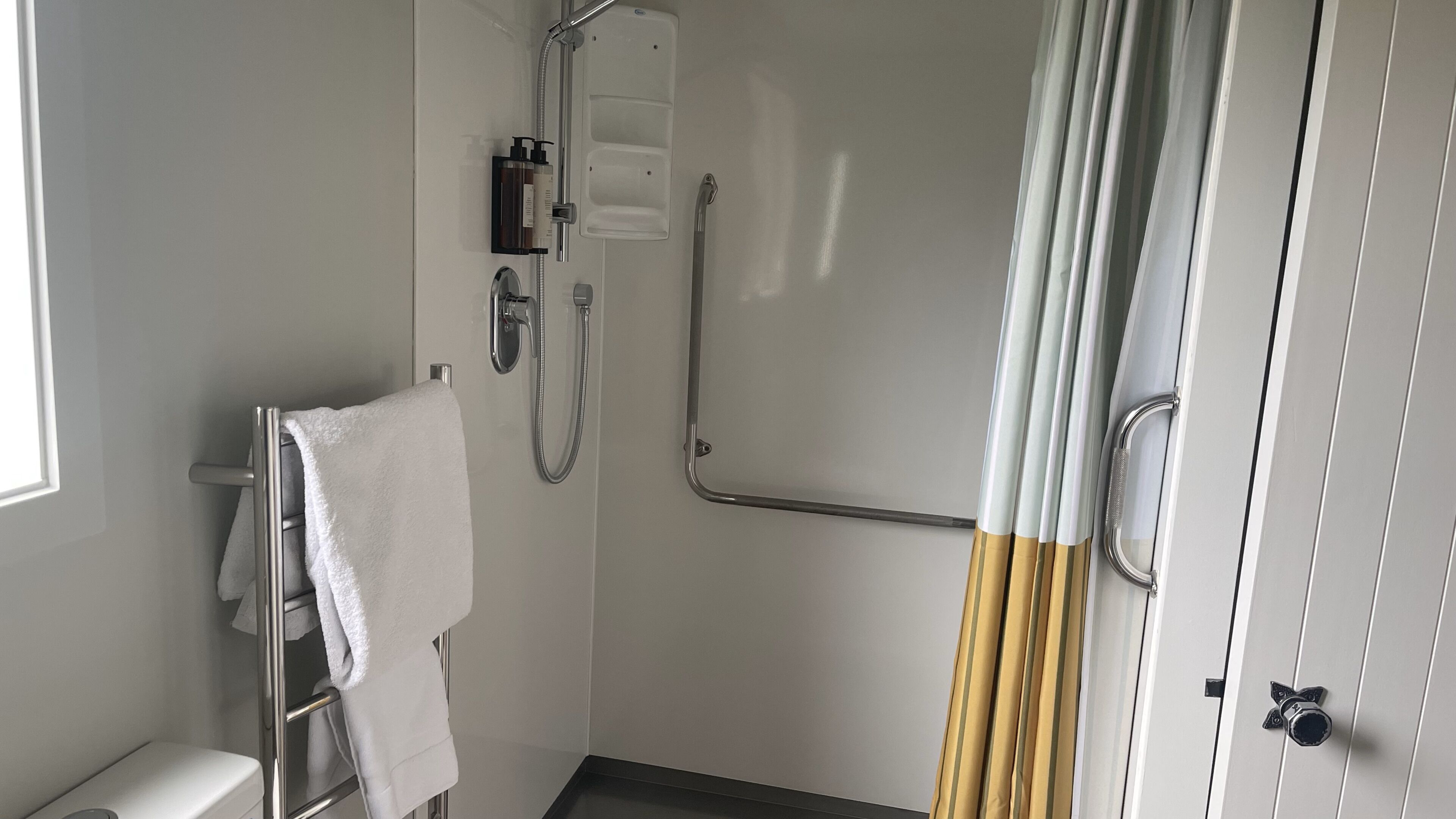 A small, modern bathroom with a shower, a toilet, and a towel rack.