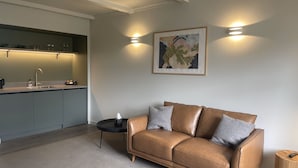 Una sala de estar moderna con un sofá de cuero, una mesita auxiliar y una zona de cocina con un fregadero y armarios.