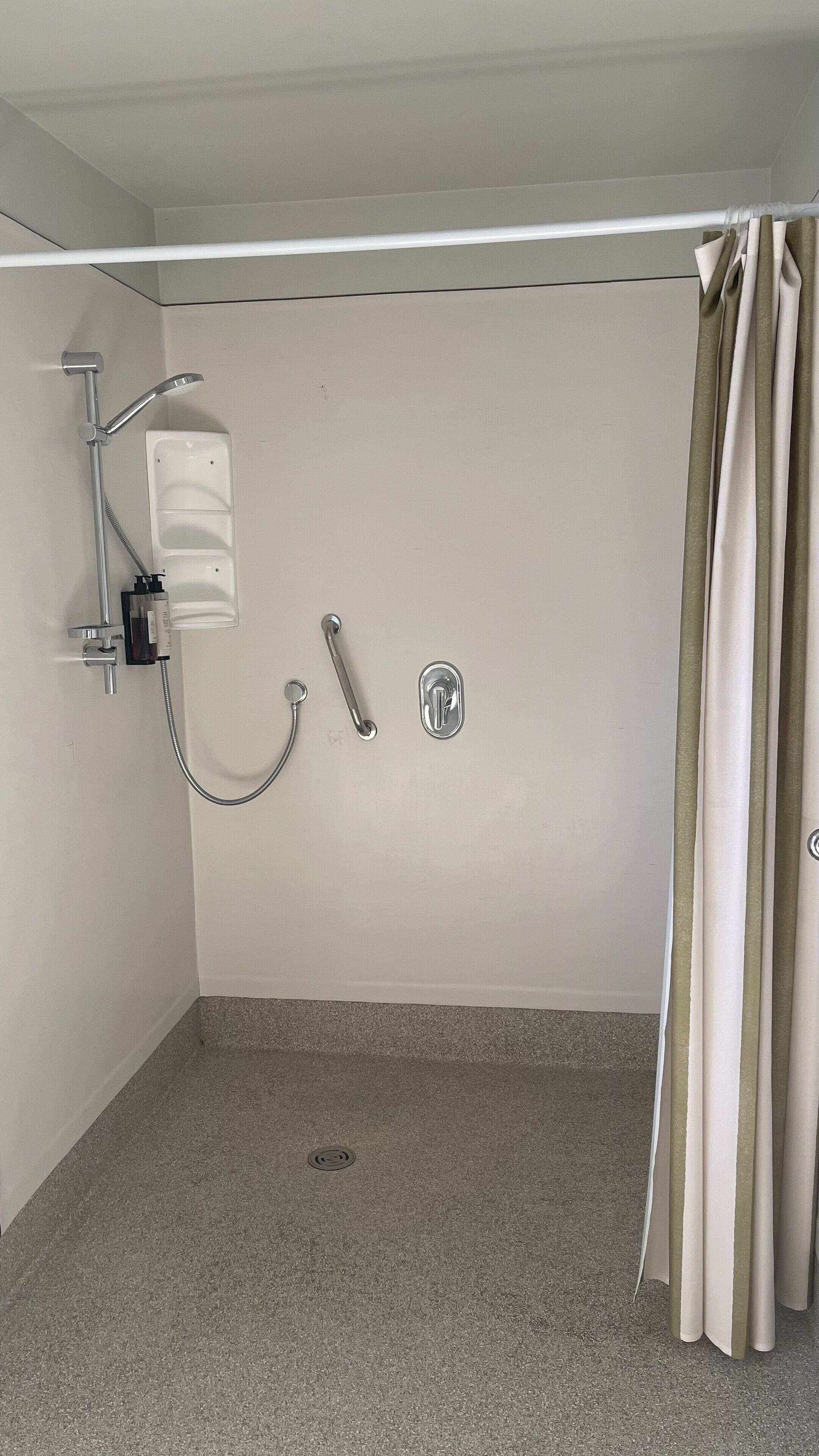 A small, enclosed shower area with a showerhead, handheld shower, and a drain.