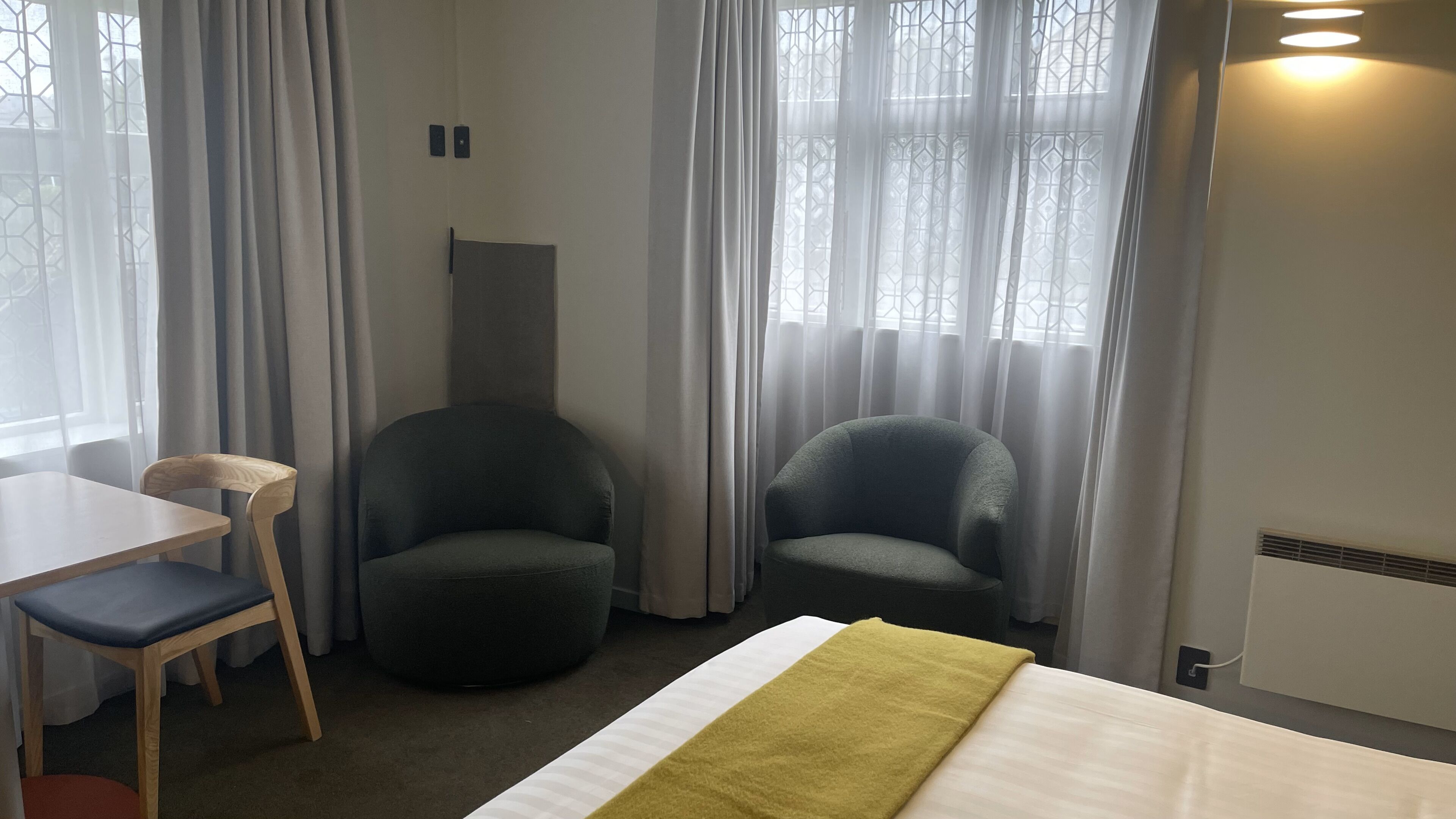 Una habitación de hotel con cama, dos sillones, un escritorio con silla y una ventana con cortinas.