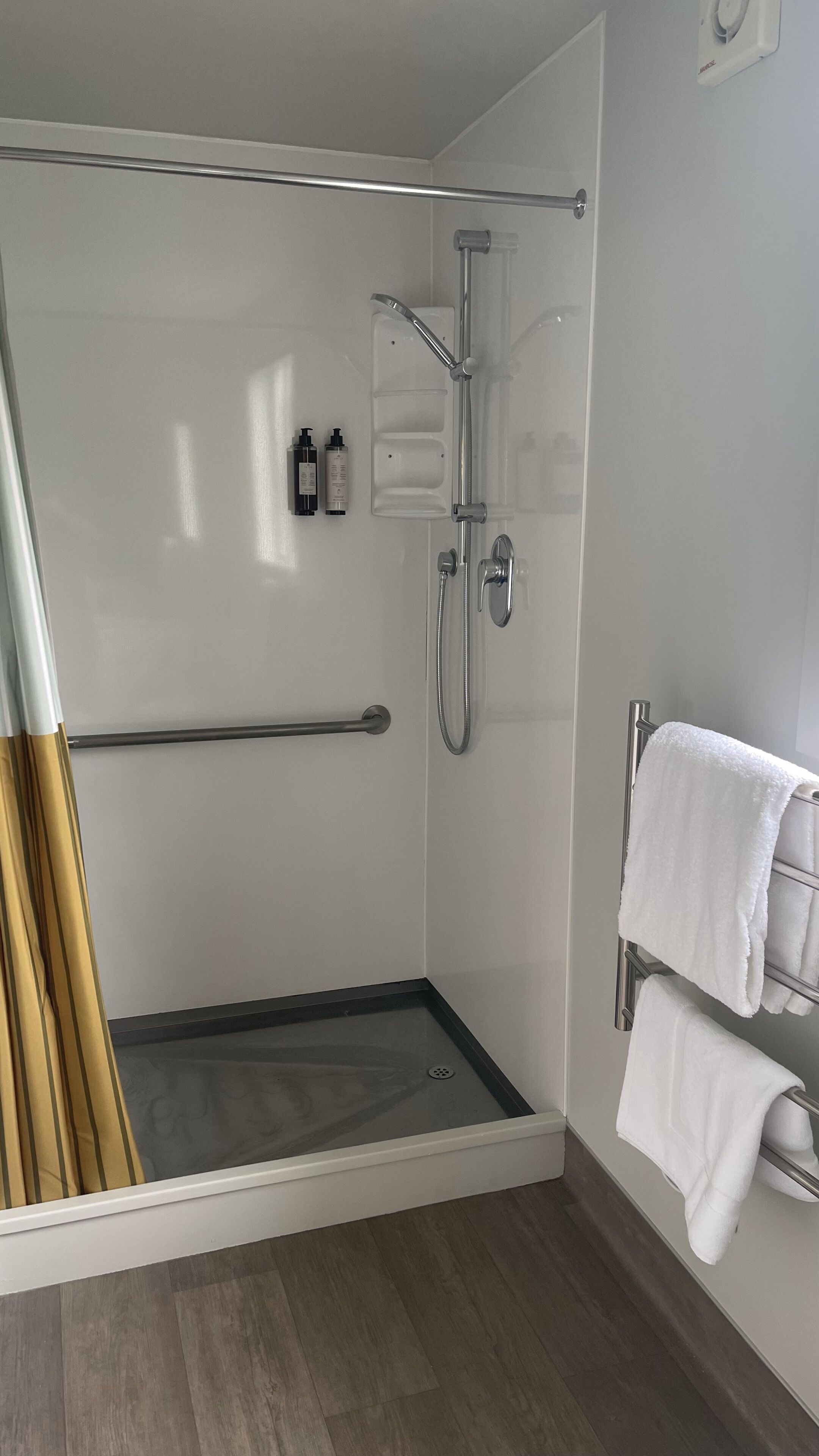 A modern bathroom with a glass-enclosed shower, a towel rack, and a wooden bath mat.