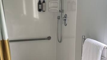 A modern bathroom with a glass-enclosed shower, a towel rack, and a wooden bath mat.