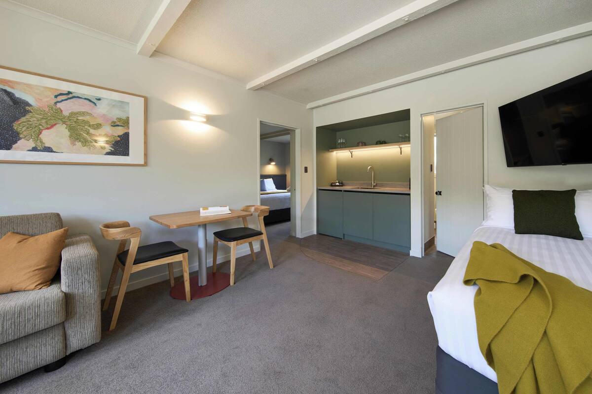 Een hotelkamer met een bed, een bank, een eettafel met stoelen, een keukenhoek en een aan de muur bevestigde televisie.