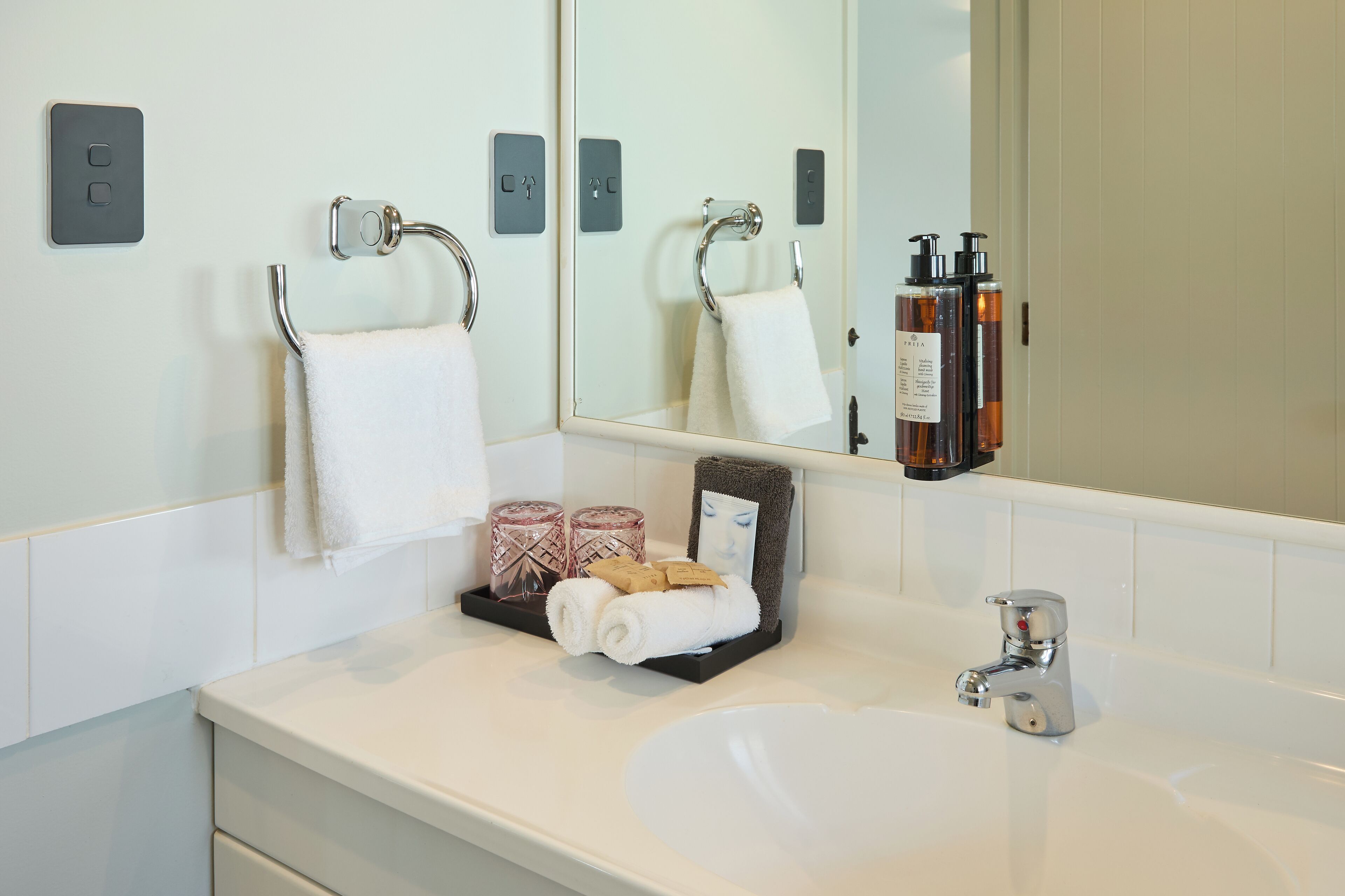 A bathroom with a white sink, a mirror, and a towel rack. There are two candles and a small tray with a towel and a picture frame.