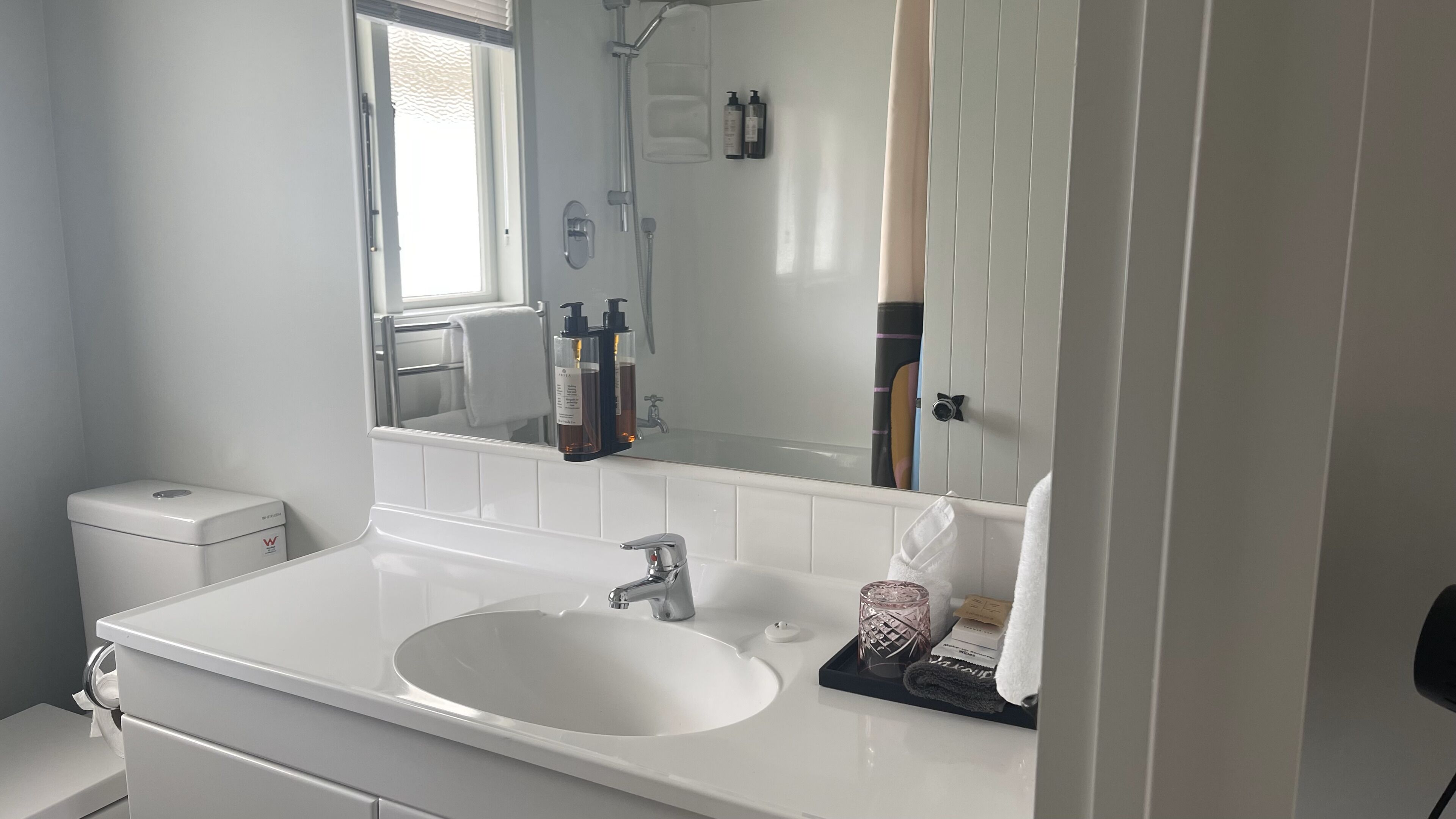 A modern bathroom with a white sink, a large mirror, and a shower area.