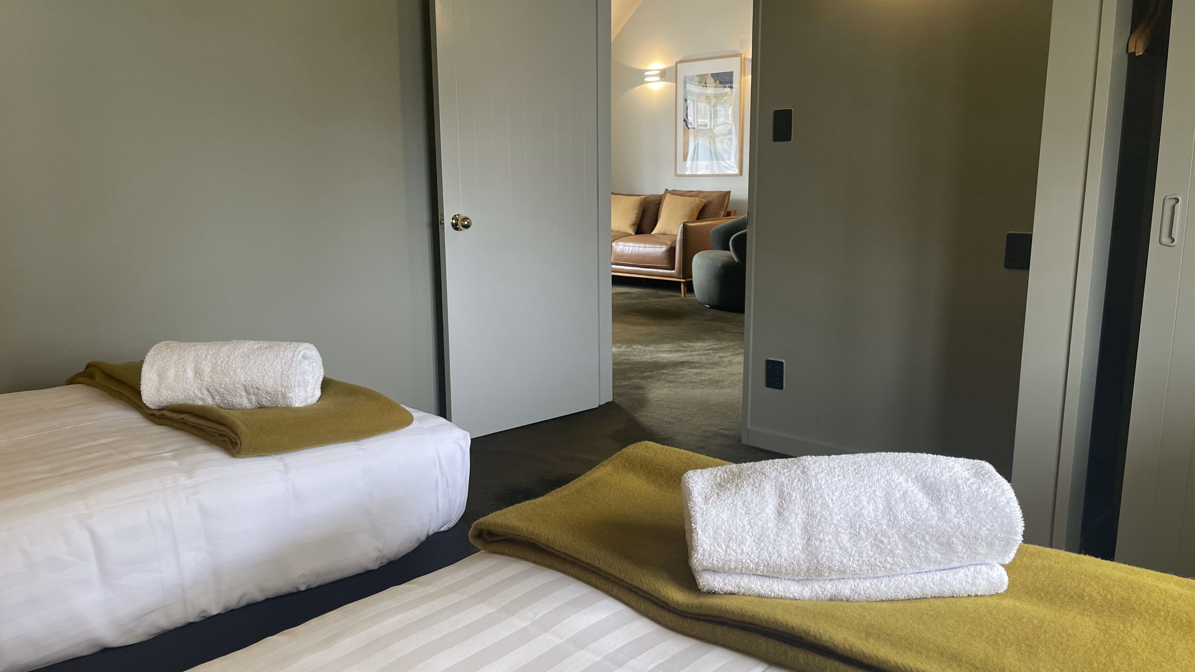A hotel room with two beds, each with a white blanket and a brown throw.