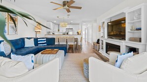 A spacious living room with a blue sofa, white armchairs, a wooden coffee table, and a fireplace. - NEW! Oceanfront! Beach Vacation Bliss! 50 Steps ToThe Sand, Pool, Great Views. (Oak Island)