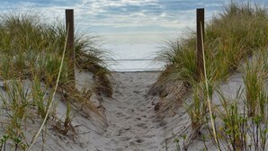 A sandy beach path flanked by grass and wooden posts leading to the sea. - NEW! Oceanfront! Beach Vacation Bliss! 50 Steps ToThe Sand, Pool, Great Views. (Oak Island)