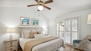 A bedroom with a bed, nightstands, a desk, a ceiling fan, and a window with blinds. - Dogs Welcome! Pool access. 1 Block to beach! Serene retreat under a majestic old oak canopy (Fernandina Beach)