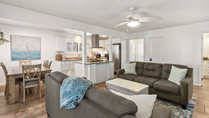 A modern living room with a gray sofa, a coffee table, and a dining area with a wooden table and chairs. - Dogs Welcome! Pool access. 1 Block to beach! Serene retreat under a majestic old oak canopy (Fernandina Beach)