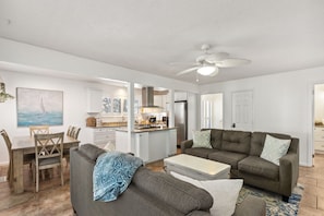 A modern living room with a gray sofa, a coffee table, and a dining area with a wooden table and chairs.