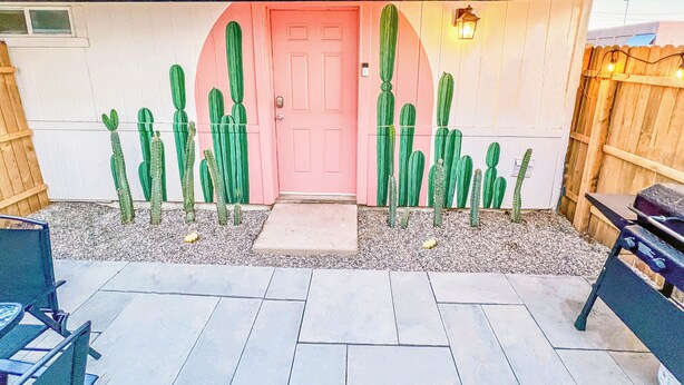 A house with a pink door, a wooden fence, and several cacti.