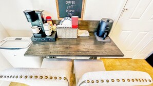 A small kitchen with a coffee maker, a toaster, and a kettle on the counter. There is a chalkboard with the words "Coffee first people later" on it.