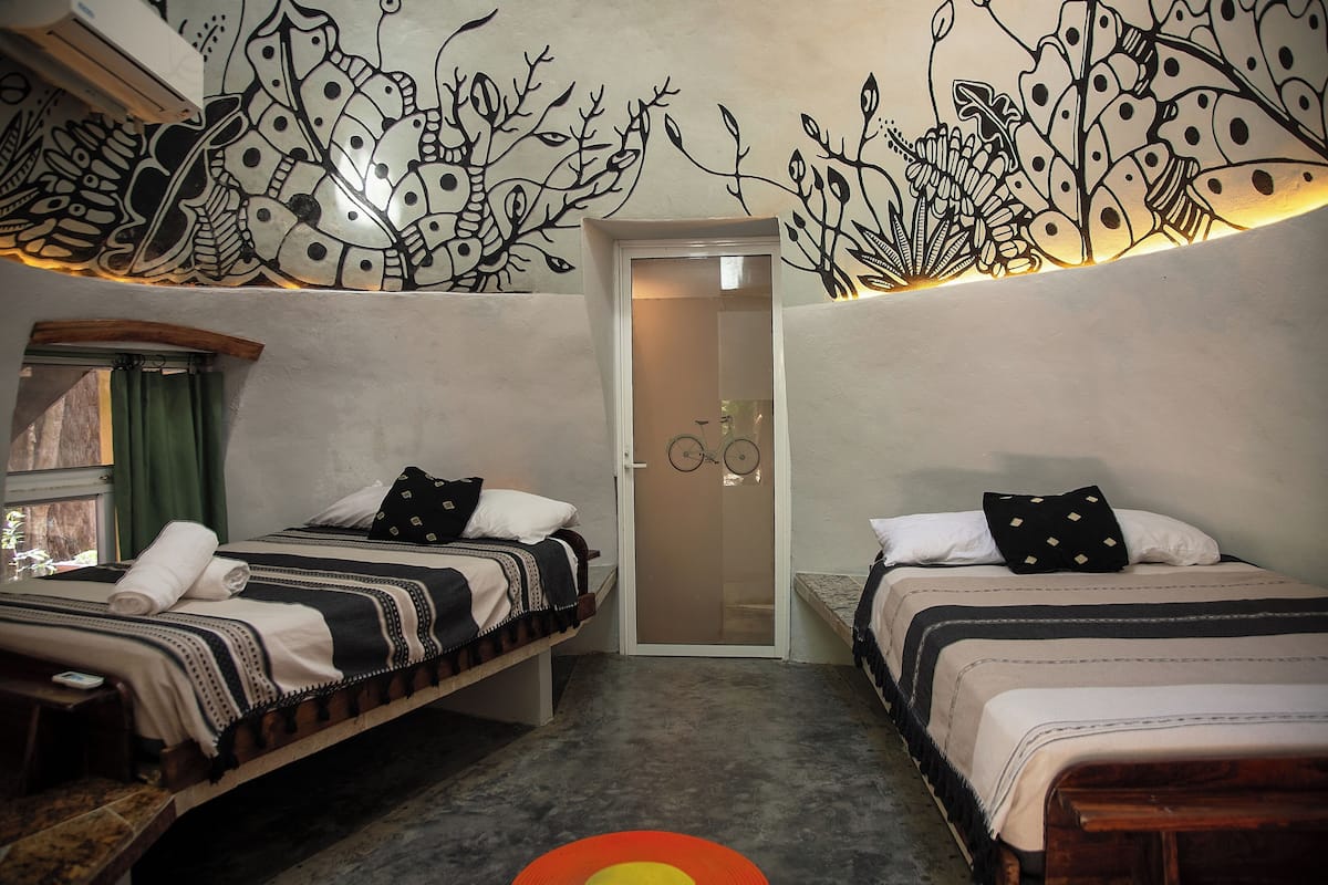 Quarto com duas camas, uma bicicleta na entrada e um mural na parede.