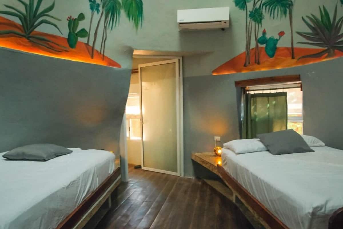 Quarto com duas camas, piso de madeira e porta que dá para outro espaço.